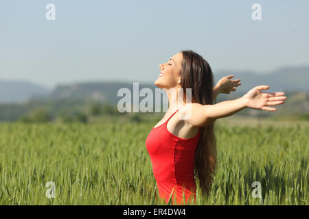 Donna respirazione profonda aria fresca nel verde di un campo di grano che indossa una maglietta rossa Foto Stock