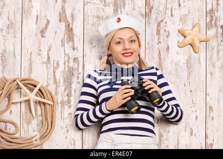 Marinaio femmina giacente su un ponte con un binocolo in mano e guardando la telecamera Foto Stock