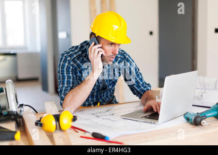 Uomo che parla al telefono cellulare e utilizzando laptop sul lato della costruzione. Pilzno, Polonia Foto Stock