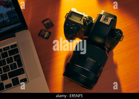 Ancora la vita delle fotocamere DSLR, sdhc memorie flash e il computer portatile su un tavolo di legno. Elevato angolo di visione degli oggetti con la luce del tramonto Foto Stock