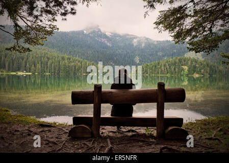 Giovane donna seduta su una panchina guardando attraverso il Lago Nero Crno Jezero nel Parco Nazionale del Durmitor, Zabljak, Montenegro, Western Foto Stock