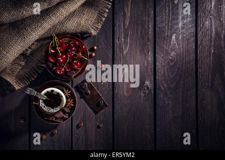 Tazza di caffè, cioccolato fondente e ciliegie sul tavolo di legno Foto Stock