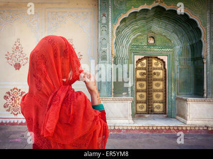 La donna in sciarpa rossa guardando il cancello verde porta in palazzo di città di Jaipur, Rajasthan, India Foto Stock