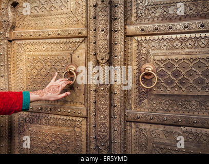 Donna con la mano di pittura henné apertura porta d'oro nel palazzo di città di Jaipur, Rajasthan, India Foto Stock