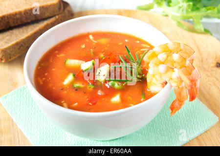 Deliziosi piatti gustosi piatti di verdura fredda zuppa di pomodoro gazpacho con gamberi (gamberetti) e rosmarino in vaso bianco su sfondo di legno, chiudi Foto Stock