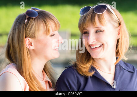 Graziosi gemelli ragazze divertimento all'aperto d'estate il parco. Giovane studente sorelle ridere parlare di ogni altro Foto Stock