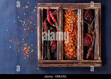 Assortimento di tutto asciutte e scaglie red hot chili peppers in una scatola di legno su blu scuro tela come sfondo Foto Stock
