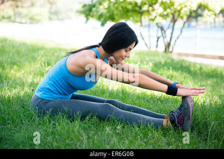 Bella donna sportiva stretching su erba verde in posizione di parcheggio Foto Stock