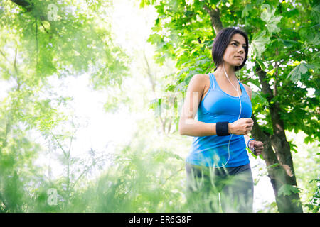 Bella donna fitness nelle cuffie in esecuzione all'aperto nel parco. Guardando lontano Foto Stock