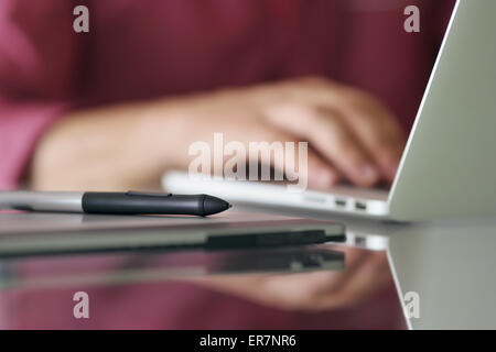 Fotografo digitando sulla tastiera del computer portatile. Primo piano della tavoletta digitale e penna stilo in primo piano Foto Stock