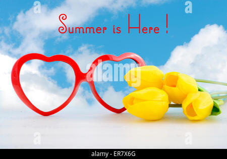 L'estate è qui concetto con cuore rosso forma di occhiali da sole e fiori di colore giallo su bianco tavolo in legno e cielo blu sullo sfondo. Foto Stock