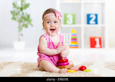 Carino baby giocando con colorate piramide giocattolo a casa Foto Stock