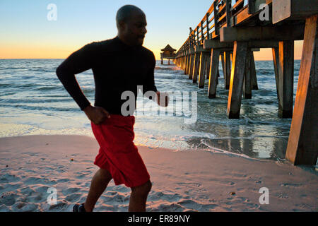 Uomo che corre sulla spiaggia al tramonto Foto Stock