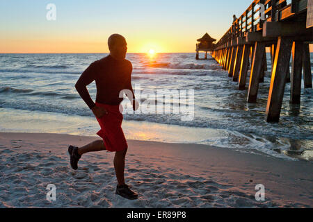 Uomo che corre sulla spiaggia al tramonto Foto Stock