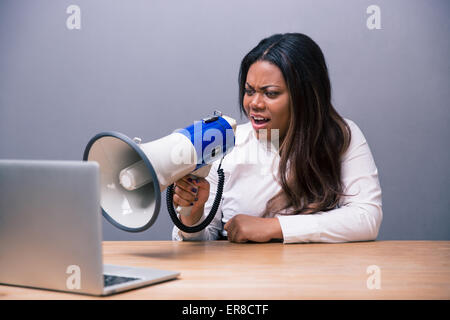 Imprenditrice africana seduti a tavola e urlando nel megafono su laptop Foto Stock