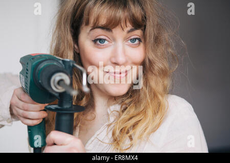 Ritratto di fiducioso giovane donna holding trapano a casa Foto Stock