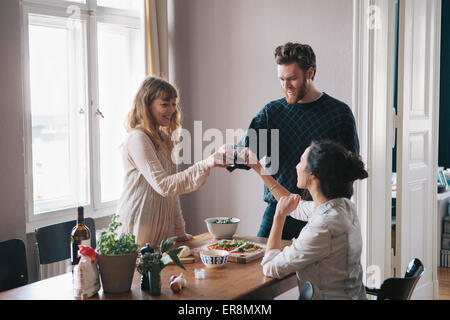 Giovane uomo con amici di sesso femminile Come tostare il vino in casa Foto Stock