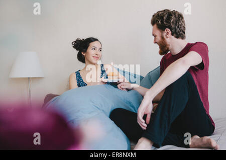Felice giovane donna azienda tortina di compleanno con candela mentre guardando l'uomo sul letto Foto Stock
