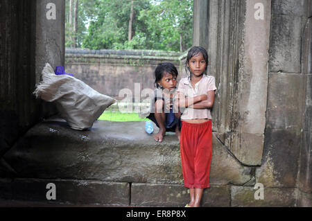 Ragazze cambogiane resto dalla raccolta di bottiglie di acqua tenendo riparo dalla pioggia a Angkor Wat in Siem Reap, Cambogia. Foto Stock