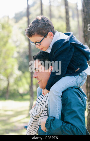 Uomo sorridente figlio che porta sulle spalle in foresta Foto Stock