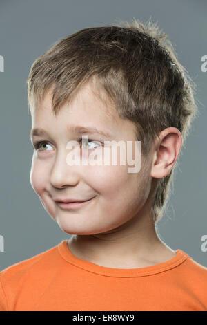 Close-up di sorridere Ragazzo che guarda lontano contro lo sfondo grigio Foto Stock