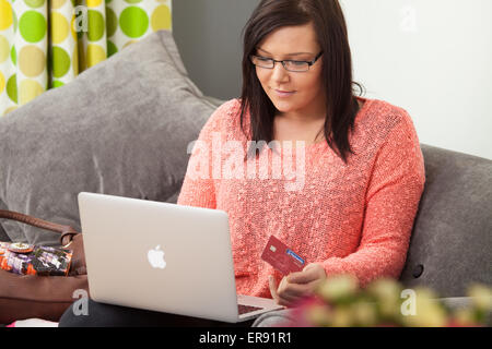 Giovane donna seduta a casa utilizzando un computer portatile per lo shopping online. Foto Stock
