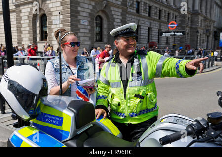 Un traffico maschio funzionario di polizia di colore giallo brillante giacca con alta potenza in moto a parlare con una giovane donna, Londra, Inghilterra. Foto Stock