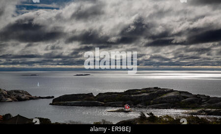 Il sole le danze in tutta l'acqua con un cielo tempestoso in Norvegia fiordo, con un colore rosso brillante cabina con un piccolo yacht Foto Stock