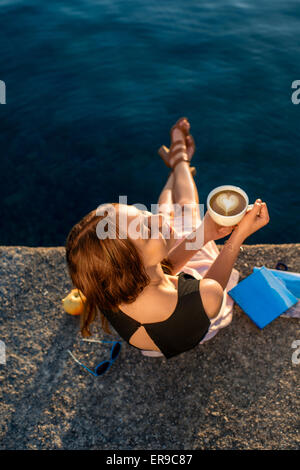 Giovane donna seduta sul molo di sunrise Foto Stock