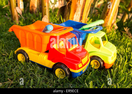 Colorato giocattolo di plastica carrelli in erba a simboleggiare la costruzione e il trasporto nel commercio Foto Stock