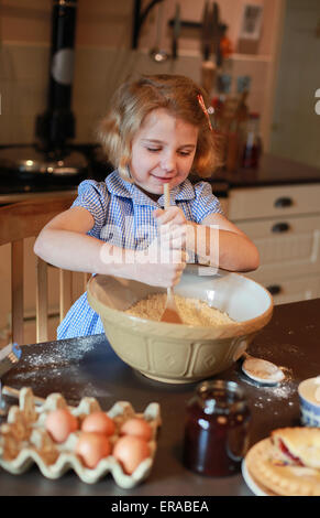 Bella bionda ragazza dai capelli miscelare gli ingredienti in una ciotola per un grafico a torta Foto Stock