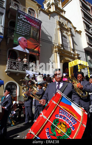 La Paz, Bolivia, 30 maggio 2015. Una banda di ottoni passa uno striscione di Papa Francesco appeso fuori dal Santuario di El Señor del Gran Poder durante le sfilate per il Gran Poder Festival. Papa Francesco visiterà la Paz durante la sua gita di 3 giorni in Bolivia, prevista per luglio 2015. Il festival in onore di El Señor del Gran Poder si svolge oggi ed è il più grande festival di la Paz. Foto Stock