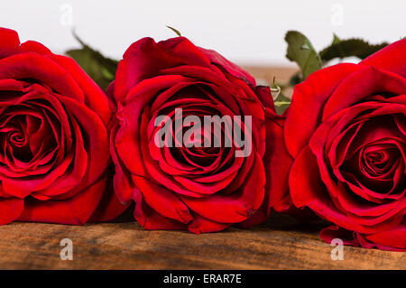 Tre rose rosse in fila su di un tavolo di legno Foto Stock