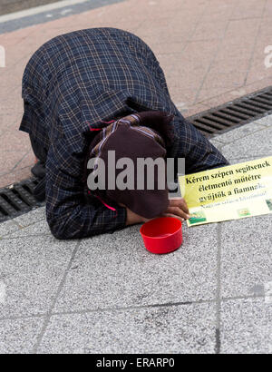 Una donna anziana è di accattonaggio sul terreno di una delle strade principali di Budapest, Ungheria. Foto Stock