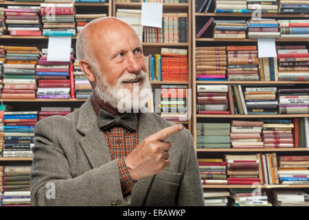 Il Professor iProfessor nella biblioteca di libri sullo sfondo puntando al themn la biblioteca di libri di puntamento di sfondo Foto Stock