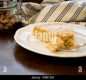 Dolci fatti in casa torta al limone con le mandorle e la farina di avena, vaso di vetro con le mandorle, fetta con la forcella sulla piastra bianca, vecchio tavolo in legno Foto Stock