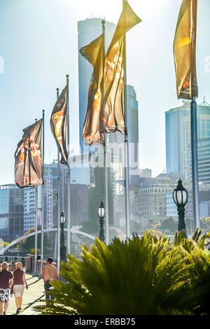 Due donna passeggiando lungo la riva del fiume, Southbank Promenade con bandiere sventolano al vento sopito luce attraverso di Melbourne Foto Stock