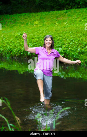 Donna anziana ballare a piedi nudi in un fiume Foto Stock