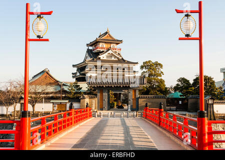 Giappone, Nagoya. Ricostruzione in calcestruzzo del ponte fluviale in legno con ringhiere e lampade vermiglio, che conduce al castello di Kiyosu con sfondo cielo blu. Foto Stock