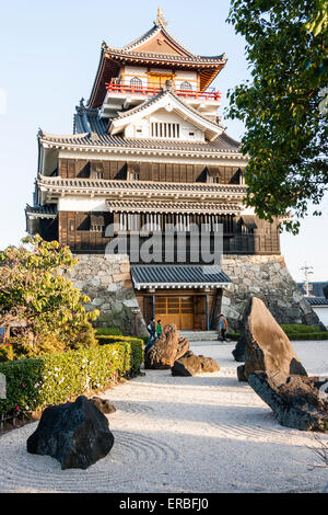 Giappone, Nagoya, ricostruito castello Kiyosu, con un castello in stile Borogata tenere il sole contro cielo blu chiaro. In primo piano un giardino in pietra giapponese. Foto Stock