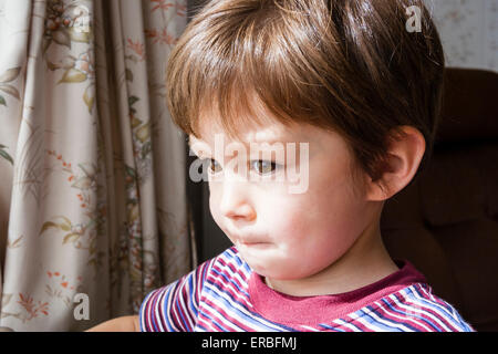 Primo piano colpo di testa di faccia di bambino, ragazzo, 4-5 anni, con capelli marroni con espressione facciale che suggerisce che è sconcertato e pensando profondamente. Foto Stock