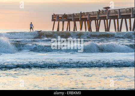 Florida surfer godendo un sunrise surf session a Jacksonville Beach presso il molo. Foto Stock