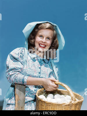 Negli anni quaranta anni cinquanta sorridente ragazza adolescente che indossa la ragazza di fattoria PIONEER OUTFIT ABITO CALICO COFANO cestello di contenimento di uova Foto Stock