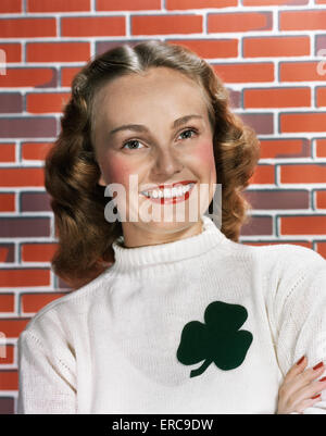 Negli anni quaranta anni cinquanta ritratto sorridente donna che indossa un maglione BIANCO CON SHAMROCK DESIGN guardando la fotocamera Foto Stock