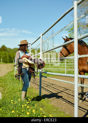 Cowgirl portante una sella di cavallo in un paddock Foto Stock