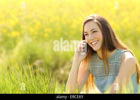 Donna chiamando al telefono cellulare in un campo verde con fiori di colore giallo Foto Stock