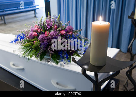 Una bara con un omaggio floreale in un obitorio e una candela che brucia Foto Stock