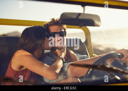 Amare giovane coppia in viaggio. Donna bacia il fidanzato guance. Giovane uomo alla guida di un'auto. Romantico coppia giovane godendo Foto Stock