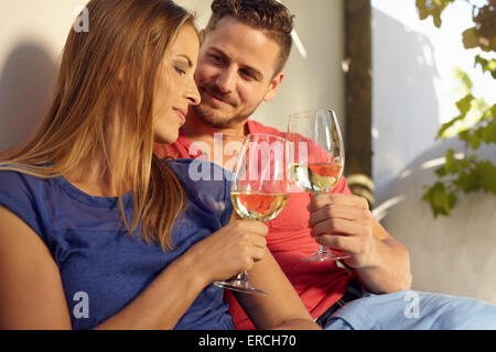 Coppia giovane celebrando con vino bianco, insieme all'esterno. Giovane uomo e donna come tostare il bicchiere di vino seduti vicino togethe Foto Stock