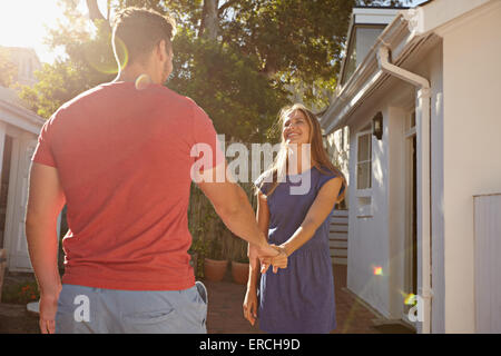 Felice giovane donna tenendo la mano del suo ragazzo e passeggiate intorno a casa loro. Amorevole coppia giovane esterni nel loro cortile o Foto Stock